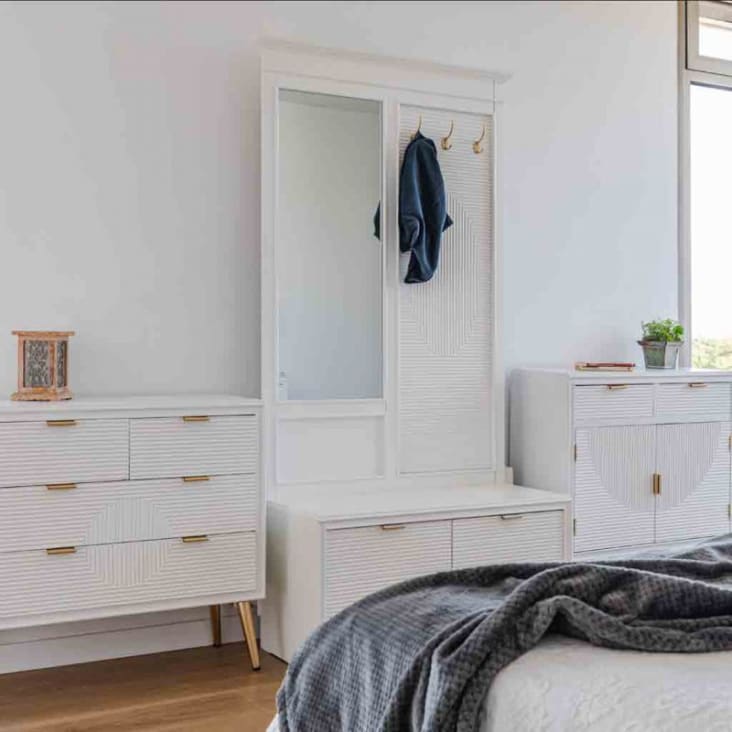 Un dormitorio blanco con una cómoda blanca y una cómoda blanca con cuadros  en la pared.